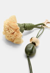 Pärlknipplad nyckelring med en blomma i krämfärgad crepe-papper, grön texturerad stam och glansiga guld- och mörkgröna pärlor.