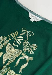 Zielony bawełniany t-shirt z różnymi złotymi wzorami kokard w różnych kształtach i wzorach, z paskowanym oznaczeniem na dekolcie.