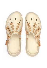 Zapatos de plástico beige tipo chanclas con agujeros recortados y detalles tejidos en marrón; presenta un acento floral. Suela texturizada y logo de la marca en el interior.