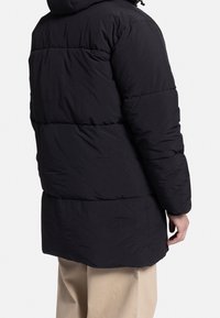 Schwarzer, gepolsterter Wintermantel mit Kapuze, mit horizontalen Steppnähten und einem leicht verlängerten Schnitt. Glatte Oberfläche und elastische Bündchen.