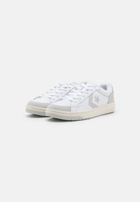 White sneakers with grey suede accents, featuring a textured white leather upper, round toe, lace-up closure, and a rubber sole.