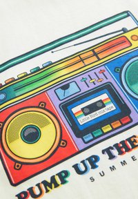 Grafika ar krāsainu boomboksu, kurā ir dzelteni un melni skaļruņi, kasešu lentes ar uzrakstu "Little Bird mix tape" un dzīvīgas pogas.