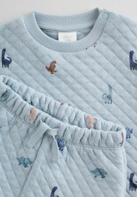 Lyseblå quiltet babytøjssæt bestående af en langærmet bluse og bukser med elastisk talje. Pyntet med farverige dinosaurtryk hele vejen igennem.