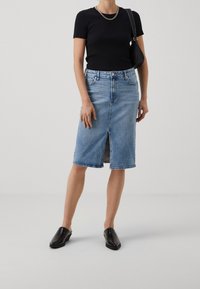 Jeanskjol i ljusblå med framsprund, hög midja och mindre slitningar. Kombinerad med en svart figurnära topp och svarta slip-on skor.