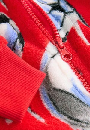 Punane fliisist ühes tükis, millel on täispikk tõmblukk, soonitud mansetid ja sinised, valged ning mustad abstraktsed mustrid. Pehme tekstuur, mugav disain.