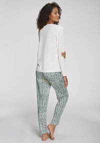 Haut blanc à manches longues à coupe ample associé à un pantalon rayé vert et blanc, doté d'une texture lisse et de détails de motif subtils.
