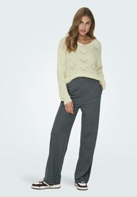 Maglione crema a maglia con motivo a zigzag e vestibilità rilassata, abbinato a pantaloni grigi larghi e sneakers scure con accenti bianchi.