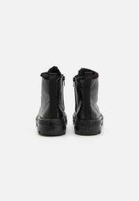 Black ankle boots with a textured leather finish, plush interior lining, and elastic side panels. Flat rubber soles with subtle branding detail.