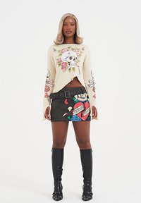 Suéter corto crema con diseño de calavera y flores; falda mini negra con vibrantes patrones de flores y corazones; botas negras hasta la rodilla.