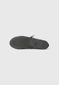 Sandale en mesh noire avec une semelle en caoutchouc texturé, dotée d'une sangle ajustable et d'un design élégant et moderne.