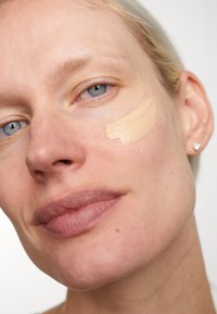 Foundationkräm i ljusbeige applicerad med ett drag på huden. Den lena texturen kontrasterar med den naturliga hudtonen. Subtil, klar hy.
