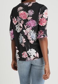 Blouse noire à manches courtes ornée de motifs floraux vibrants dans des teintes de rose, blanc et bleu ; tissu doux avec une coupe décontractée.
