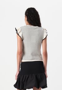 Strikket topp med svart-hvite striper, korte volangermer og en strukturert overflate. Kombinert med et svart skjørt med utvidet nederkant.
