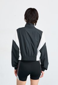 Veste coupe-vent noir et blanc avec un col haut, une taille élastique et des manches longues, assortie à un short noir. Texture de tissu lisse.