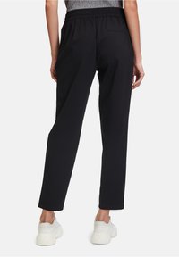 Pantalon de sport noir avec une taille élastique, design à jambes droites et une poche arrière unique. Fabriqué en tissu doux et flexible.