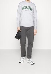 Szara bluza z zielonym napisem "JACK&JONES", połączona z szarymi spodniami cargo i białymi sneakersami. Czarna torba trzymana w lewej ręce.