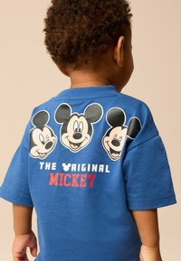 Blå bomulds T-shirt med tre Mickey Mouse grafik på ryggen, med teksten "THE ORIGINAL" i hvid og "MICKEY" i rød.