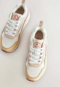 Baskets blanches et beiges en tissu en maille, avec des semelles en caoutchouc et des accents pastel contrastés. Présente un logo "Fun Times" sur la languette.