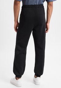 Sorte sweatpants med elastisk talje og tætsiddende manchetter. Lavet af blødt stof med en afslappet pasform. Båret med hvide sneakers.