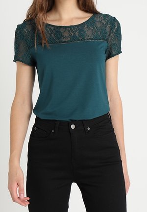 Türkisfarbener Oberteil mit kurzen Spitzenärmeln, Rundhalsausschnitt und figurbetontem Design, kombiniert mit schwarzen, hoch taillierten Jeans. Glatte Textur mit zartem Spitzenakzent.