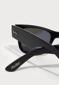 Ochelari de soare Ray-Ban negri cu lentile întunecate, având un design elegant, textură minimă și semnătura gravată "AWGE" pe brațul lateral.