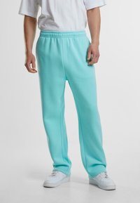 Light blue sweatpants with an elastic waistband, straight cut, side pockets, and soft texture, worn with white sneakers and a basic white shirt.