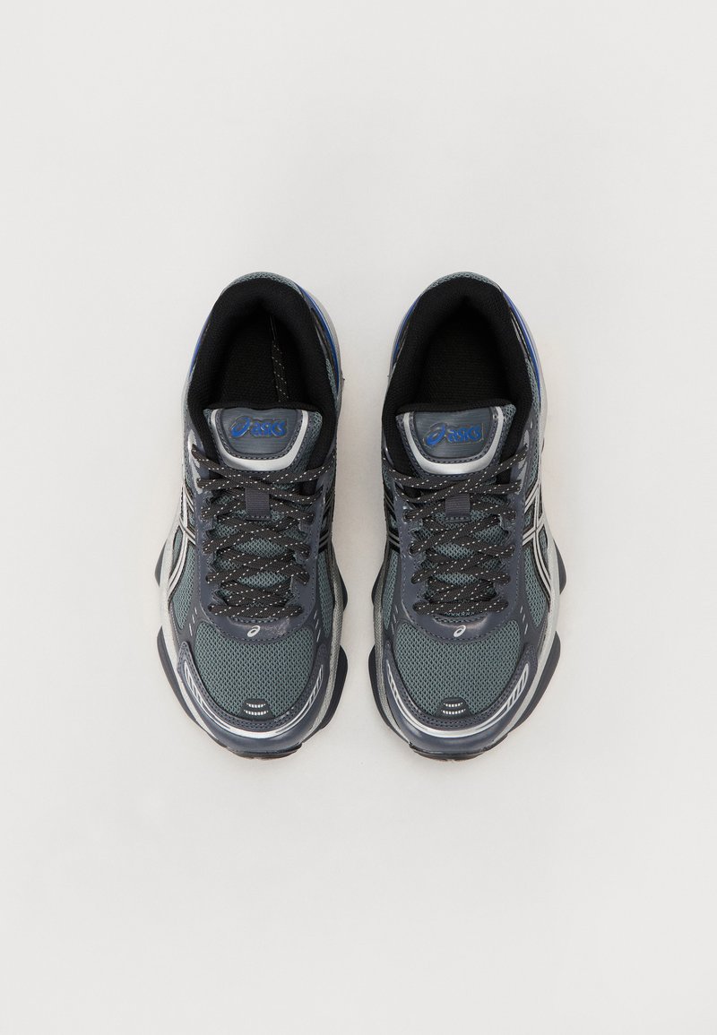 Zapatillas de running para hombres en gris oscuro y malla negra, con acentos plateados y marca azul. Cuentan con una suela acolchada y diseño de cordones.