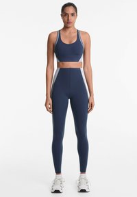 Marineblauwe sportbeha en hoge taille legging set met contrasterende zijpanelen. Glad materiaal met een getailleerd ontwerp en geen zichtbare patronen.