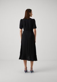 Black mid-length dress with short puff sleeves, tie waist detail, and a flared hem, paired with blue heeled shoes. Smooth fabric texture.