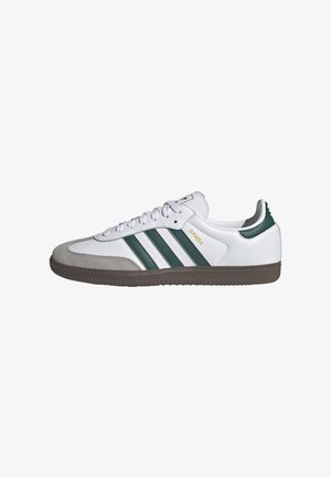 Biały sneaker Adidas Samba z zielonymi paskami, szarą zamszową czubą, brązową podeszwą i białymi sznurowadłami widziany z boku.