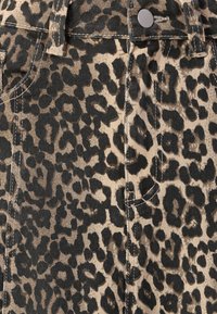 Țesătură cu imprimeu de leopard pe un fundal bej și pete negre. Prezintă cusături vizibile și un buton metalic la talie.