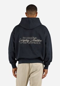 Navy hoodie with a relaxed fit, featuring white text on the back: "SUCCESS IS BUILT EVERYDAY AMBITION ON DAILY DETERMINATION."