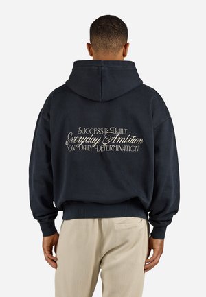 Navy hoodie with a relaxed fit, featuring white text on the back: "SUCCESS IS BUILT EVERYDAY AMBITION ON DAILY DETERMINATION."