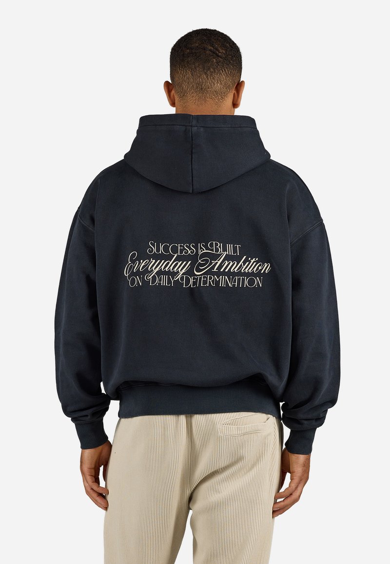Navy hoodie with a relaxed fit, featuring white text on the back: "SUCCESS IS BUILT EVERYDAY AMBITION ON DAILY DETERMINATION."