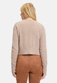 Pull beige raccourci en tissu doux avec des manches longues et un ourlet côtelé, associé à un pantalon en daim marron.