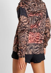 Hoodiejacka med ett virvlande mönster i brunt och korall, tillverkad av lätt material med elastiska manschetter och en avslappnad passform.