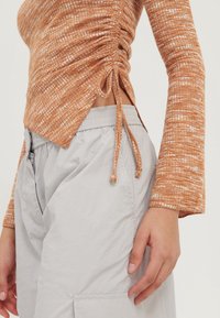 Triko s dlouhým rukávem v rezavé barvě s texturou a na bocích nařasením, doplněné světle šedými cargo kalhotami na elastický pás.