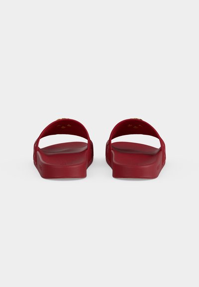 Paire de sandales slides rouges vues de dos avec de larges brides et des semelles texturées sur un fond uni.