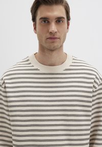 Cremfarbener Strickpullover mit dunklen horizontalen Streifen, mit Rundhalsausschnitt und lockerer Passform. Weicher Stoff und sichtbare Nähdetails.