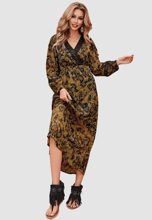 Vestido maxi con un patrón de paisley negro y dorado, mangas largas, escote en V profundo y una abertura lateral. Combinado con sandalias negras con flecos.