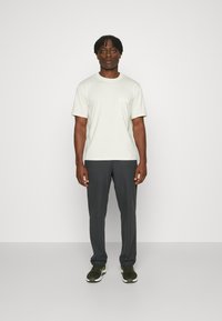 Hellgraues T-Shirt mit kurzen Ärmeln und Brusttasche, kombiniert mit dunkelgrauen Hosen und schwarzen Sportschuhen. Schlichtes Design, lässige Passform.