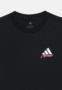 Svart bomullst-skjorte med rund hals, med en hvit Adidas-logo og rosa "Messi" tekst på venstre brystområde. Enkelt design.