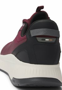 Dark burgundy sneaker with mesh upper, black rubber heel, and white outsole. Features a gray strap and minimalistic accent details.