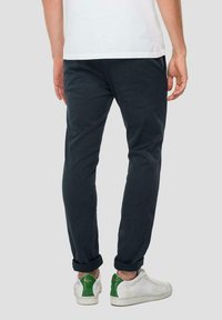 Chinos da uomo blu scuro con una vestibilità slim, orli arrotolati e una texture sottile. Indossati con sneakers bianche con accenti verdi.