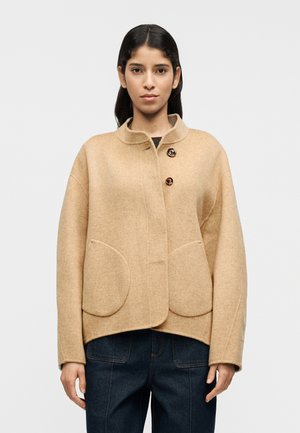 Μπεζ σακάκι από μείγμα μαλλιού με γιακά μανταρίνι, διπλό κλείσιμο με κουμπιά και στρογγυλές τσέπες με επένδυση. Φαρδιά μανίκια και άνετη εφαρμογή.