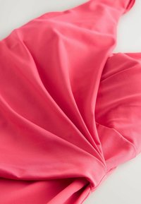 Koralų rožinės spalvos audinys su lygia tekstūra, turintis klostes ir sukimų detales. Minkšta ir tampri medžiaga, išdėstyta ant šviesaus paviršiaus.