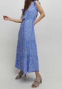 Blå blommig maxiklänning med volangärmar, knytmidja och flerfaldig kjol. I kombination med taupe blockklacksandaler med ribbade remmar.
