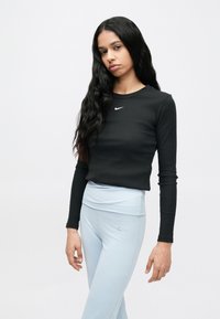 Μαύρο μακρυμάνικο τοπ με ριμπ υφή και μικρό λευκό λογότυπο Nike, συνδυασμένο με ανοιχτό μπλε κολάν ψηλόμεσο με λεπτομέρειες λογότυπου.