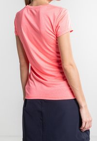 Camisa de manga corta y ligera en un vibrante color coral, con una textura suave y escote redondeado, combinada con una falda de color oscuro.