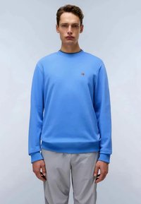 Sweatshirt azul claro feito de um tecido suave, com punhos e bainha canelados. Pequeno logo em detalhe no peito. Modelo de p�é contra um fundo simples.